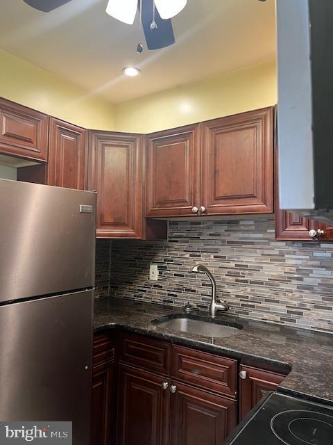 kitchen with dark stone countertops, sink, backsplash, and stainless steel refrigerator