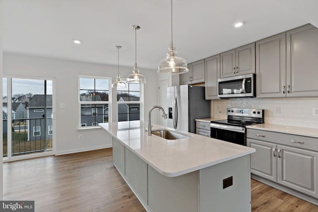 kitchen featuring gray cabinets, an island with sink, appliances with stainless steel finishes, and light stone counters