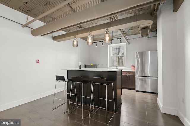 kitchen with hanging light fixtures, a kitchen island, a breakfast bar, and stainless steel refrigerator