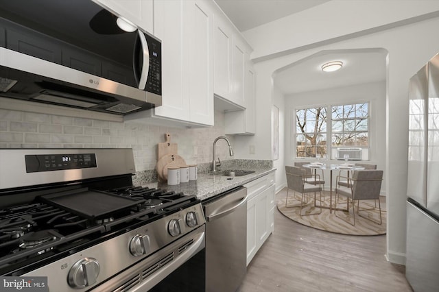 kitchen featuring sink, appliances with stainless steel finishes, white cabinetry, light stone counters, and light hardwood / wood-style floors