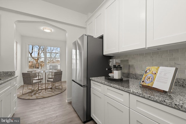 kitchen featuring backsplash, light stone countertops, light hardwood / wood-style floors, and white cabinets