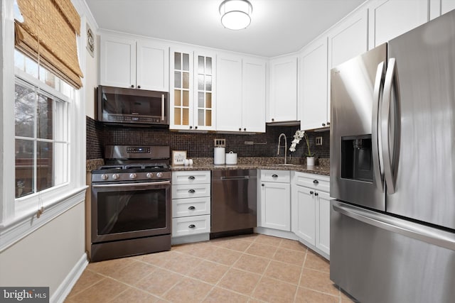 kitchen with dark stone countertops, light tile patterned floors, appliances with stainless steel finishes, white cabinets, and backsplash