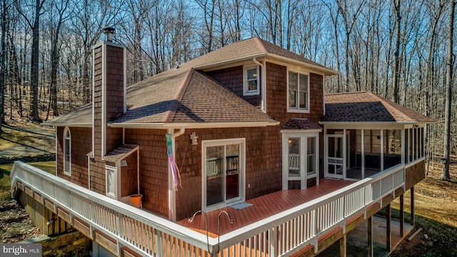 back of house with roof with shingles, a chimney, a wooden deck, and a sunroom