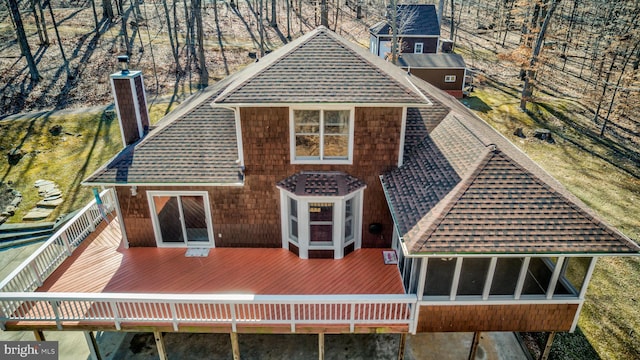 back of house featuring roof with shingles, a chimney, and a wooden deck