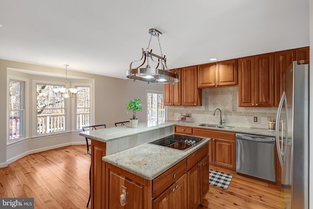 kitchen with brown cabinetry, appliances with stainless steel finishes, a sink, light wood-type flooring, and backsplash