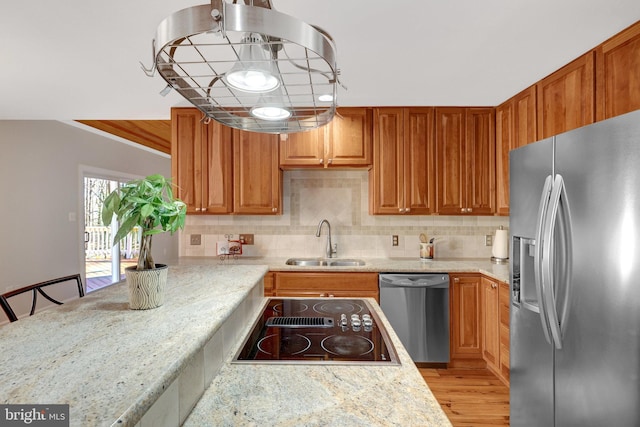 kitchen with tasteful backsplash, appliances with stainless steel finishes, light wood-style floors, brown cabinetry, and a sink