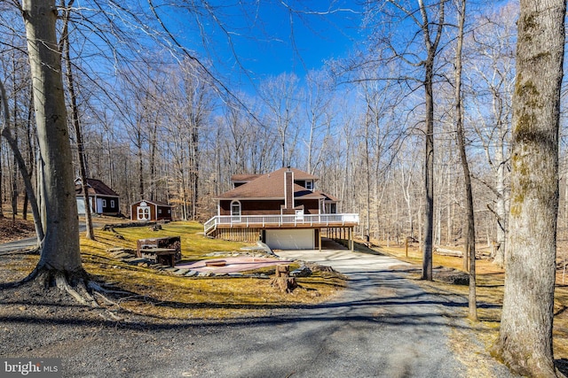 view of front of property with roof with shingles, a storage unit, an outdoor structure, driveway, and a wooden deck