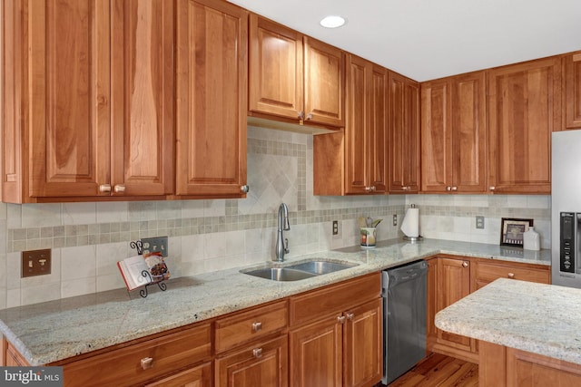 kitchen with brown cabinets, stainless steel appliances, backsplash, a sink, and light stone countertops