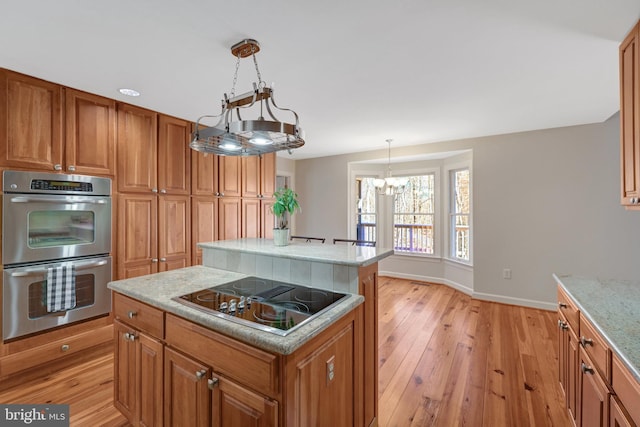 kitchen with double oven, light wood-style flooring, black electric cooktop, a kitchen island, and brown cabinets