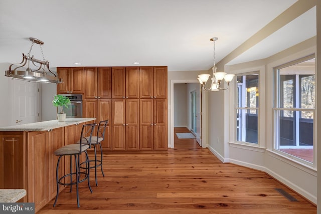 kitchen with a breakfast bar area, visible vents, stainless steel oven, light wood finished floors, and brown cabinetry