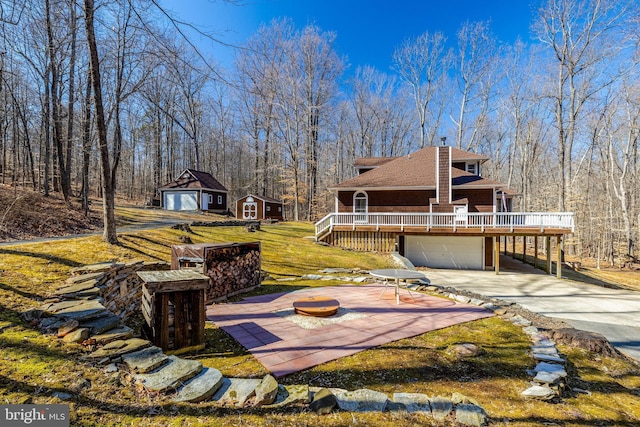 exterior space featuring an attached garage, a fire pit, an outdoor structure, driveway, and a wooden deck