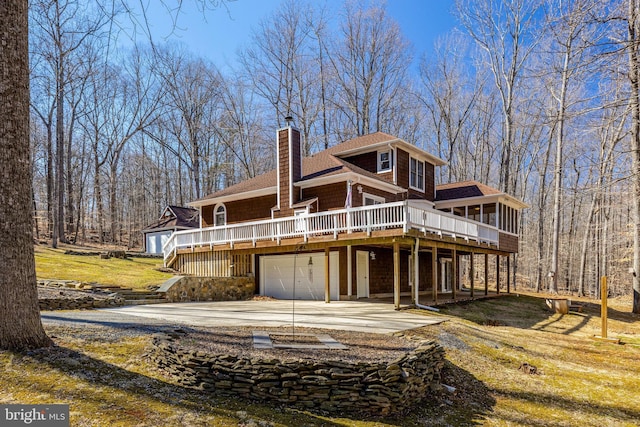 view of front of property with a shingled roof, concrete driveway, a chimney, an attached garage, and a wooden deck