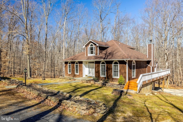 view of front of property with driveway, a shingled roof, a chimney, and a front yard