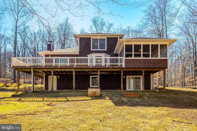 back of property with a yard, a chimney, a wooden deck, and a sunroom