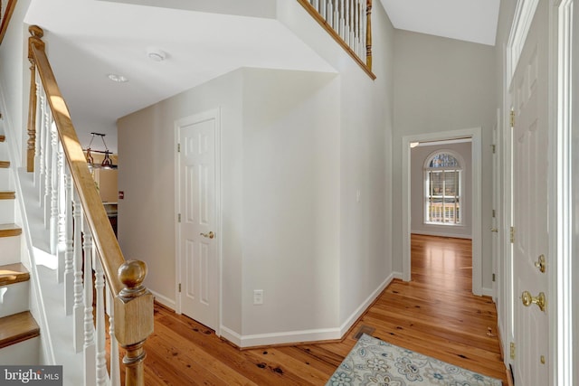 hall featuring stairs, light wood-type flooring, a towering ceiling, and baseboards