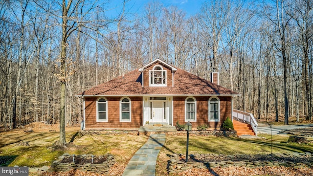 view of front of property featuring a front lawn, roof with shingles, a chimney, and a wooded view