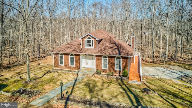 view of front of property with roof with shingles, a wooded view, a chimney, and a front lawn