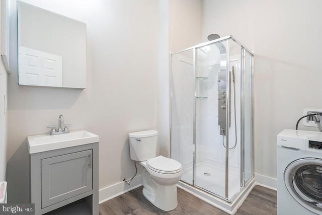 bathroom with hardwood / wood-style floors, washer / clothes dryer, vanity, toilet, and a shower with door