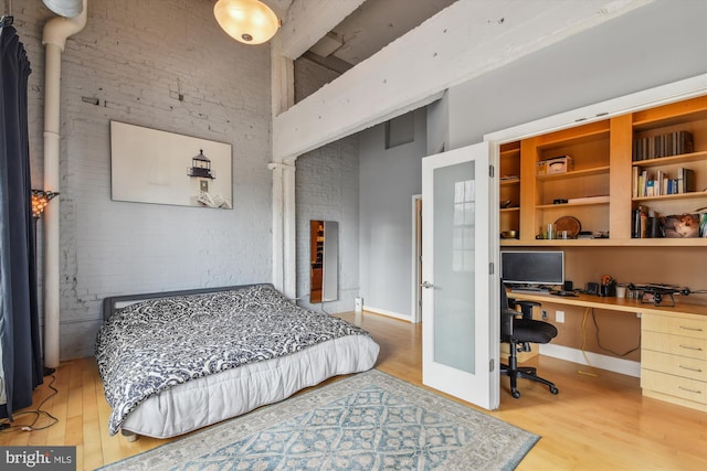 bedroom with hardwood / wood-style flooring, brick wall, built in desk, and beamed ceiling