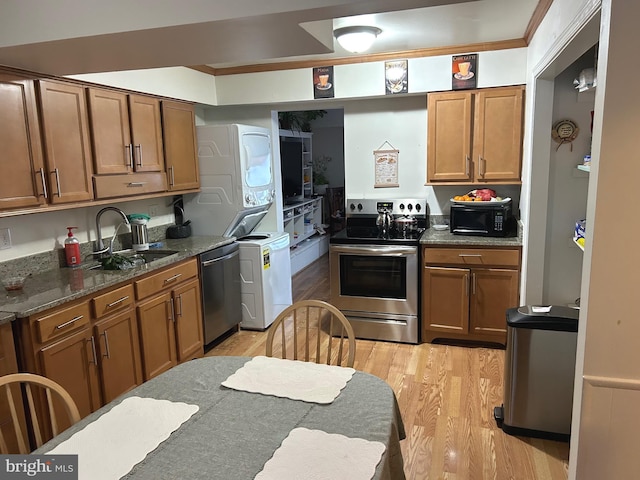 kitchen with appliances with stainless steel finishes, sink, dark stone counters, stacked washer and dryer, and light wood-type flooring