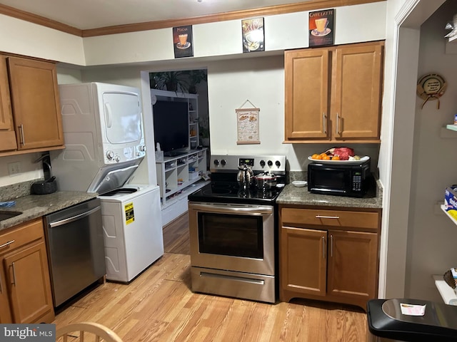 kitchen with dark stone counters, ornamental molding, stacked washer and clothes dryer, stainless steel appliances, and light hardwood / wood-style flooring