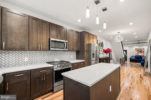 kitchen featuring tasteful backsplash, decorative light fixtures, dark brown cabinets, stainless steel appliances, and light hardwood / wood-style floors