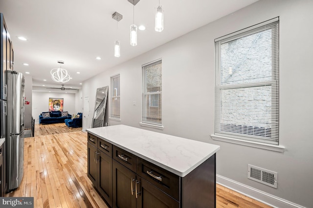 kitchen with pendant lighting, stainless steel refrigerator, dark brown cabinets, a center island, and light hardwood / wood-style floors