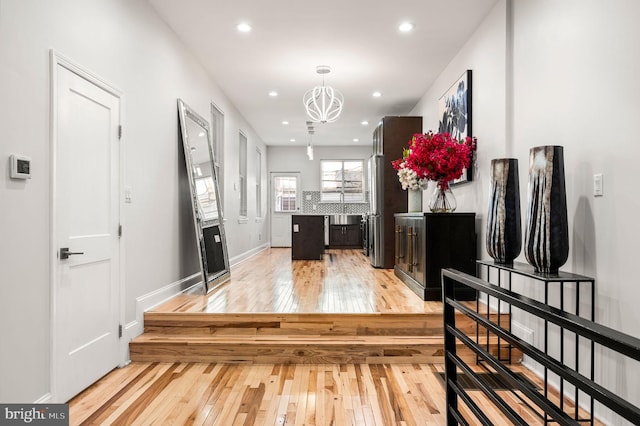 hallway with an inviting chandelier and light wood-type flooring