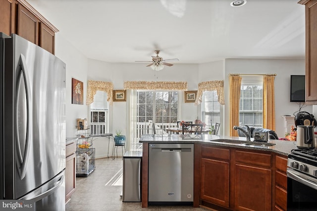 kitchen with brown cabinetry, dark stone counters, ceiling fan, a sink, and appliances with stainless steel finishes