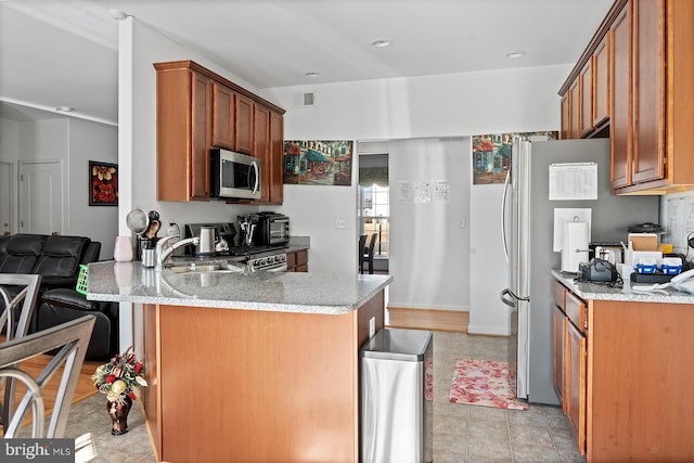 kitchen with brown cabinetry, visible vents, a peninsula, a sink, and appliances with stainless steel finishes