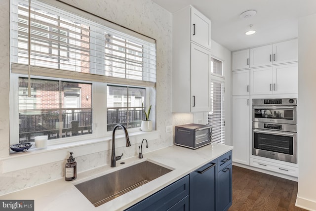 kitchen with white cabinetry, blue cabinets, double oven, and sink