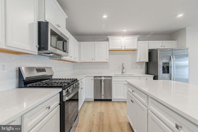 kitchen with sink, appliances with stainless steel finishes, backsplash, white cabinets, and light wood-type flooring