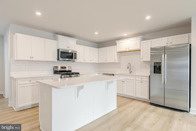 kitchen featuring sink, light hardwood / wood-style flooring, stainless steel appliances, white cabinets, and a kitchen island