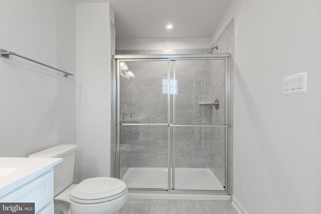 bathroom featuring a shower with door, vanity, and toilet