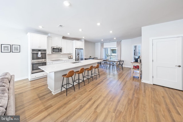 kitchen featuring light wood finished floors, an island with sink, a kitchen breakfast bar, stainless steel appliances, and white cabinetry