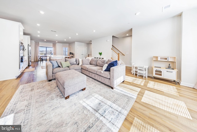 living area with visible vents, baseboards, stairs, light wood-type flooring, and recessed lighting