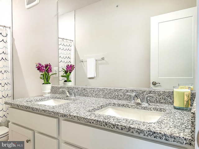 bathroom with a sink, toilet, and double vanity