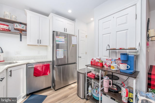 kitchen with sink, white cabinetry, appliances with stainless steel finishes, light stone countertops, and light hardwood / wood-style floors