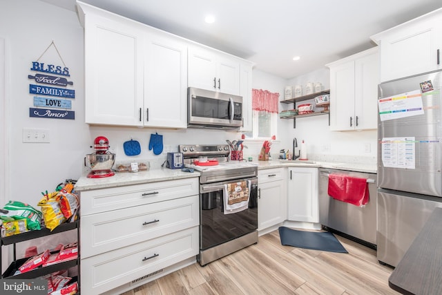 kitchen featuring appliances with stainless steel finishes, white cabinetry, sink, light stone counters, and light hardwood / wood-style floors