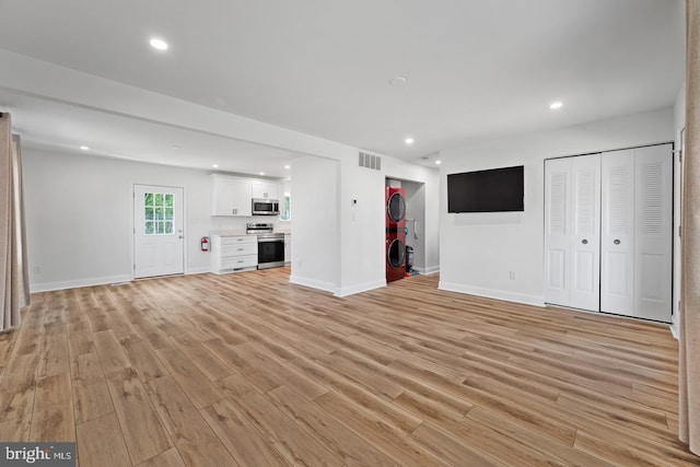 unfurnished living room with stacked washing maching and dryer and light hardwood / wood-style flooring