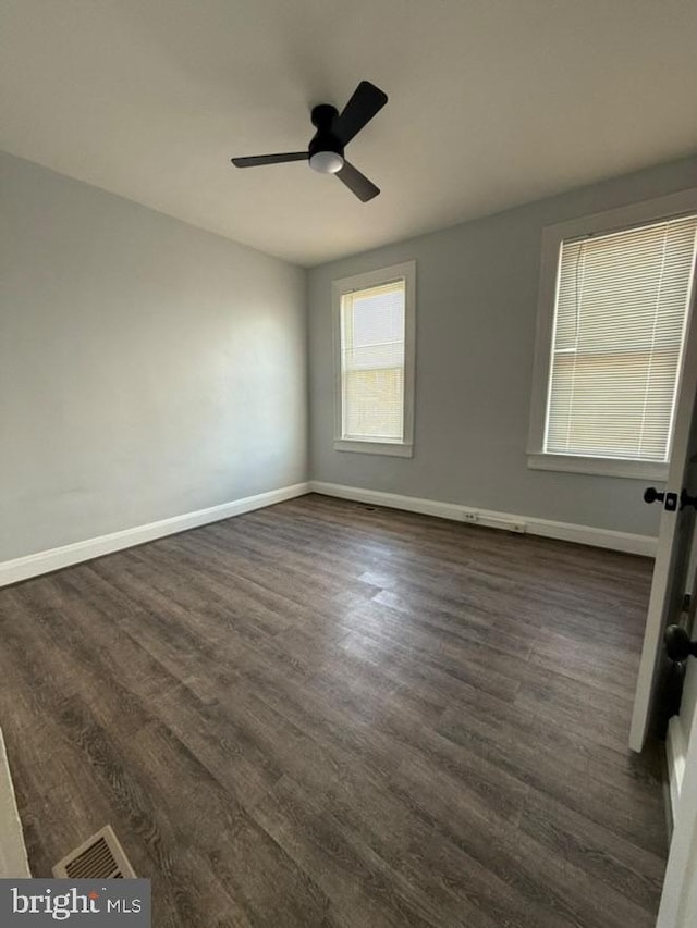 empty room with ceiling fan, dark wood-style flooring, visible vents, and baseboards