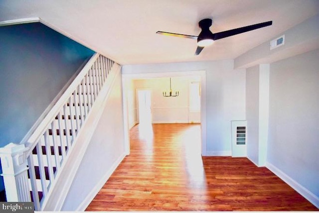 corridor with a notable chandelier, wood finished floors, visible vents, baseboards, and stairway