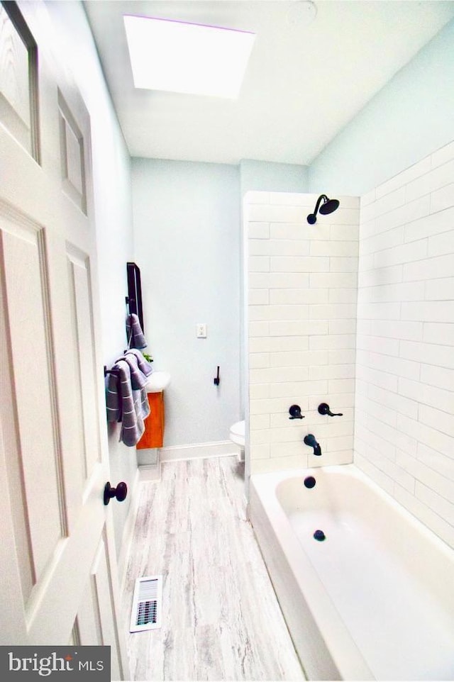 bathroom with toilet, wood finished floors, visible vents, baseboards, and shower / washtub combination