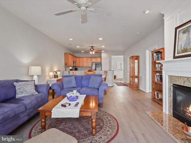 living room with ceiling fan, built in features, a high end fireplace, and light hardwood / wood-style flooring