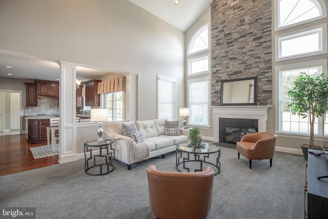 living area with baseboards, ornate columns, high vaulted ceiling, dark wood finished floors, and a fireplace