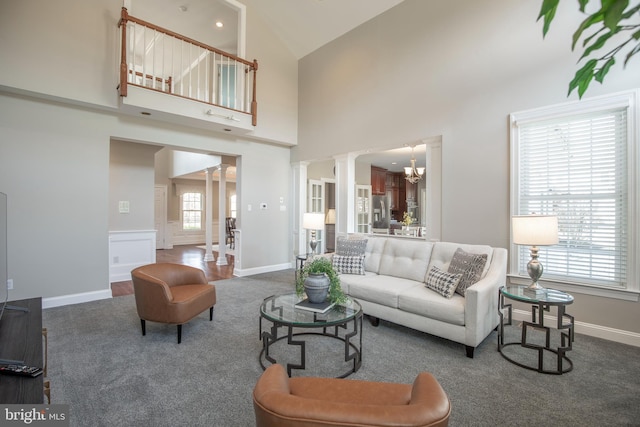 carpeted living area with a notable chandelier, wainscoting, a high ceiling, and ornate columns