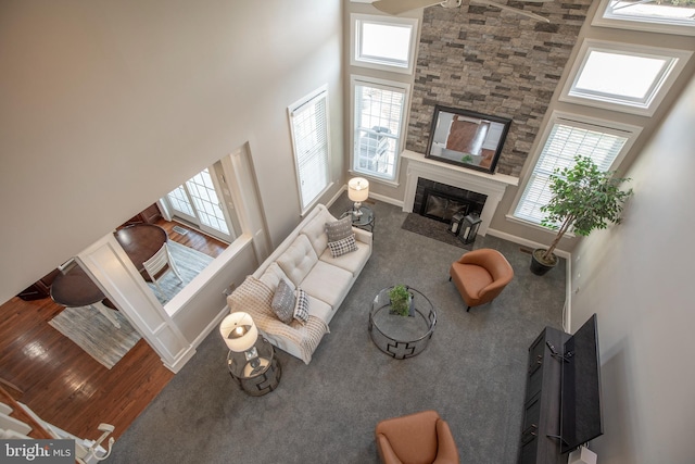 living area with wood finished floors, a high ceiling, a stone fireplace, baseboards, and ceiling fan