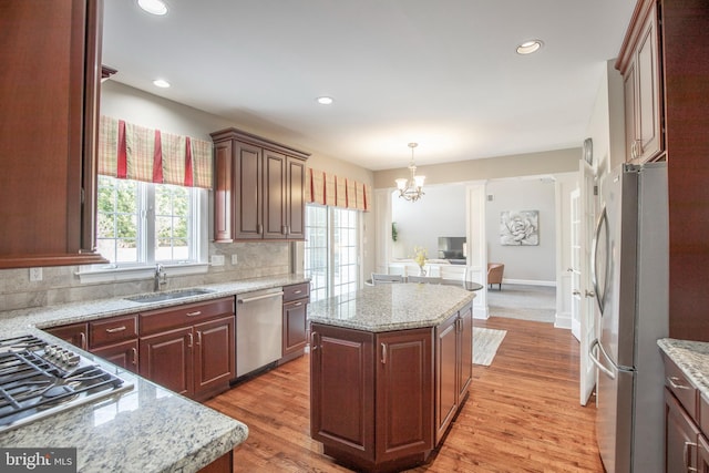 kitchen featuring a kitchen island, light wood-type flooring, a sink, appliances with stainless steel finishes, and tasteful backsplash