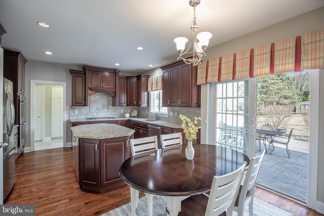 kitchen with a kitchen island, a sink, dark wood-type flooring, appliances with stainless steel finishes, and tasteful backsplash