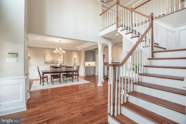 stairs with a wainscoted wall, wood finished floors, a decorative wall, decorative columns, and a chandelier